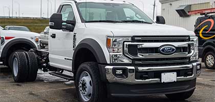 An image showing a white Ford Super Duty truck in a parking lot. The truck is equipped with an aftermarket utility service body.