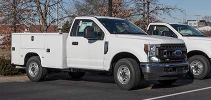 An image showing a white Ford Super Duty truck in a parking lot. The truck is equipped with an aftermarket utility service body.