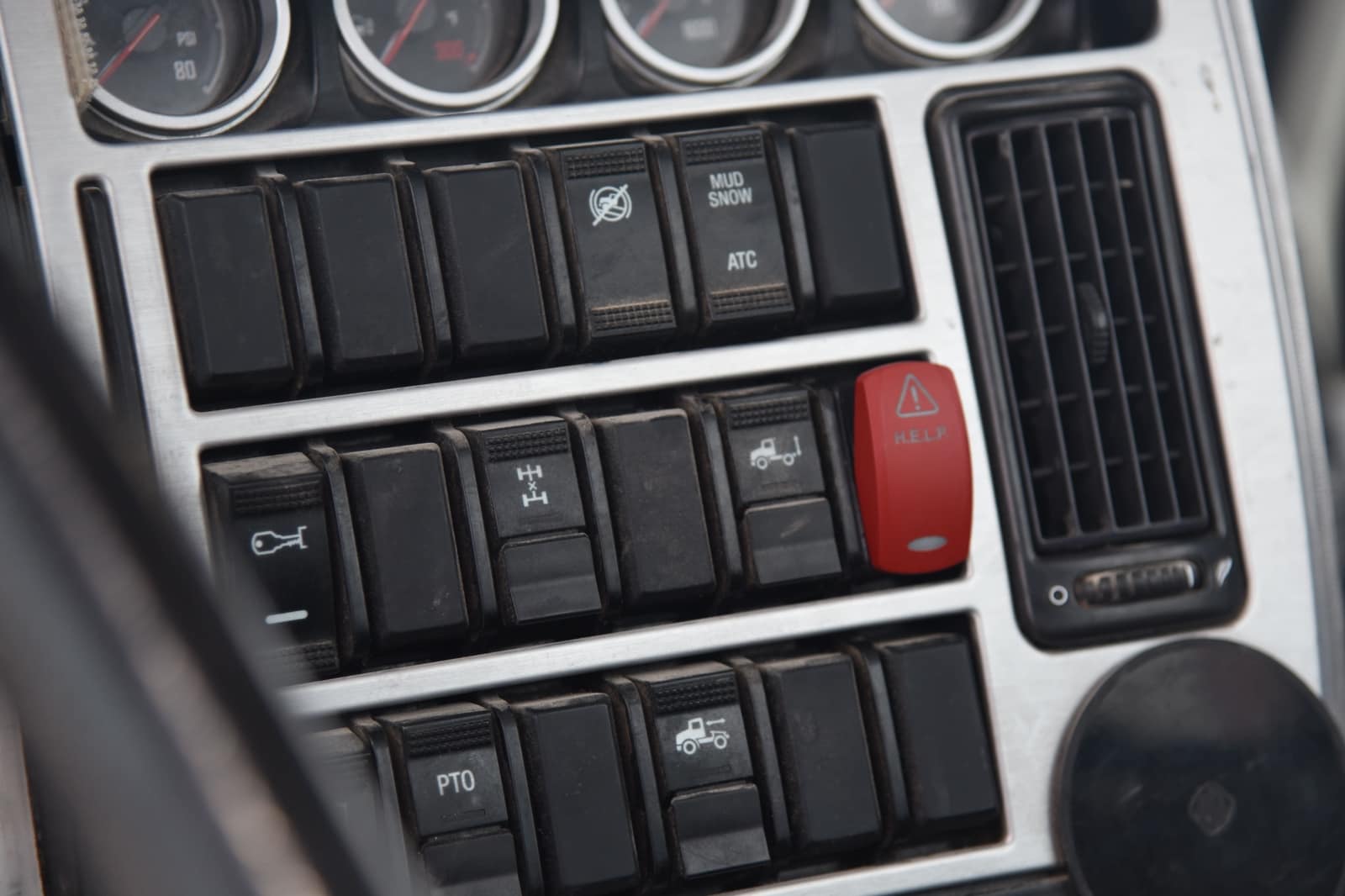 An image showing the dashboard of a heavy freight truck. In the image are multiple control switches to power on and off features of the truck. On the dashboard there is also a red button with the text H.E.L.P. to activate the VOXX HELP system upgraded flashers and commercial vehicle-to-vehicle communication system.