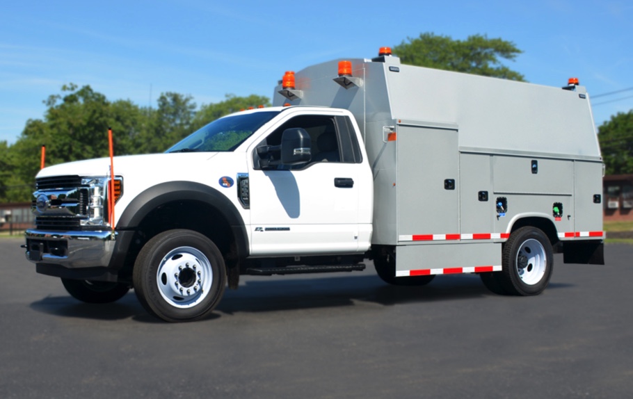 An image of a large white work truck with a gray aftermarket service body installed. The truck is outfitted with multiple strobe lamps on the exterior.