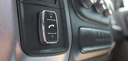 An image showing a Bluetooth control switch installed on the dashboard of a vehicle. The control switch is mounted to the surface and has icons depicting a phone and arrows that point up and down.