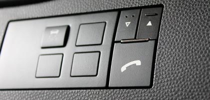 An image showing a Bluetooth control switch installed on the dashboard of a vehicle. The control switch perfectly matches the opening in the dashboard and looks original to the car. The switch has icons depicting a phone and arrows that point up and down.