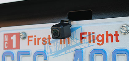 An image showing the license plate area of a vehicle. Above the license plate the head of a camera can be seen which provides backup camera functionality.