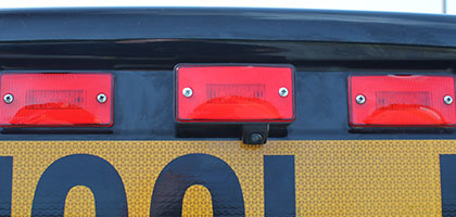 An image showing the back of a school bus. The center marker lamp of the bus has a custom assembly to hold a backup camera.