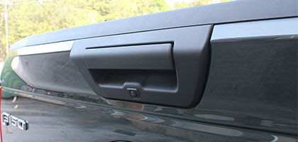 An image showing the tailgate handle of a traditional light duty truck. In the tailgate handle a camera lens is visible and provides a backup camera for the truck.
