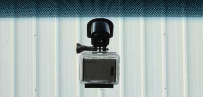 An image showing the windshield of a vehicle from the inside. In the image the rear view mirror attachment point can be seen with an action camera attached.