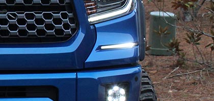An image showing the front of a blue Toyota Tundra. The focus of the image is on the area just below the Tundra's headlamp showing the Rostra bezel and DRL lamp installed.
