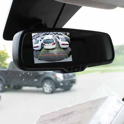 Vehicle rear view mirror with an LCD screen visible through the glass of the mirror showing video from a backup camera.
