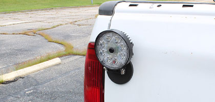 An image showing the tailgate of a truck with an LED lamp attached. In the middle of the LED lamp a camera lens can be seen which provides backup camera functionality for the vehicle.
